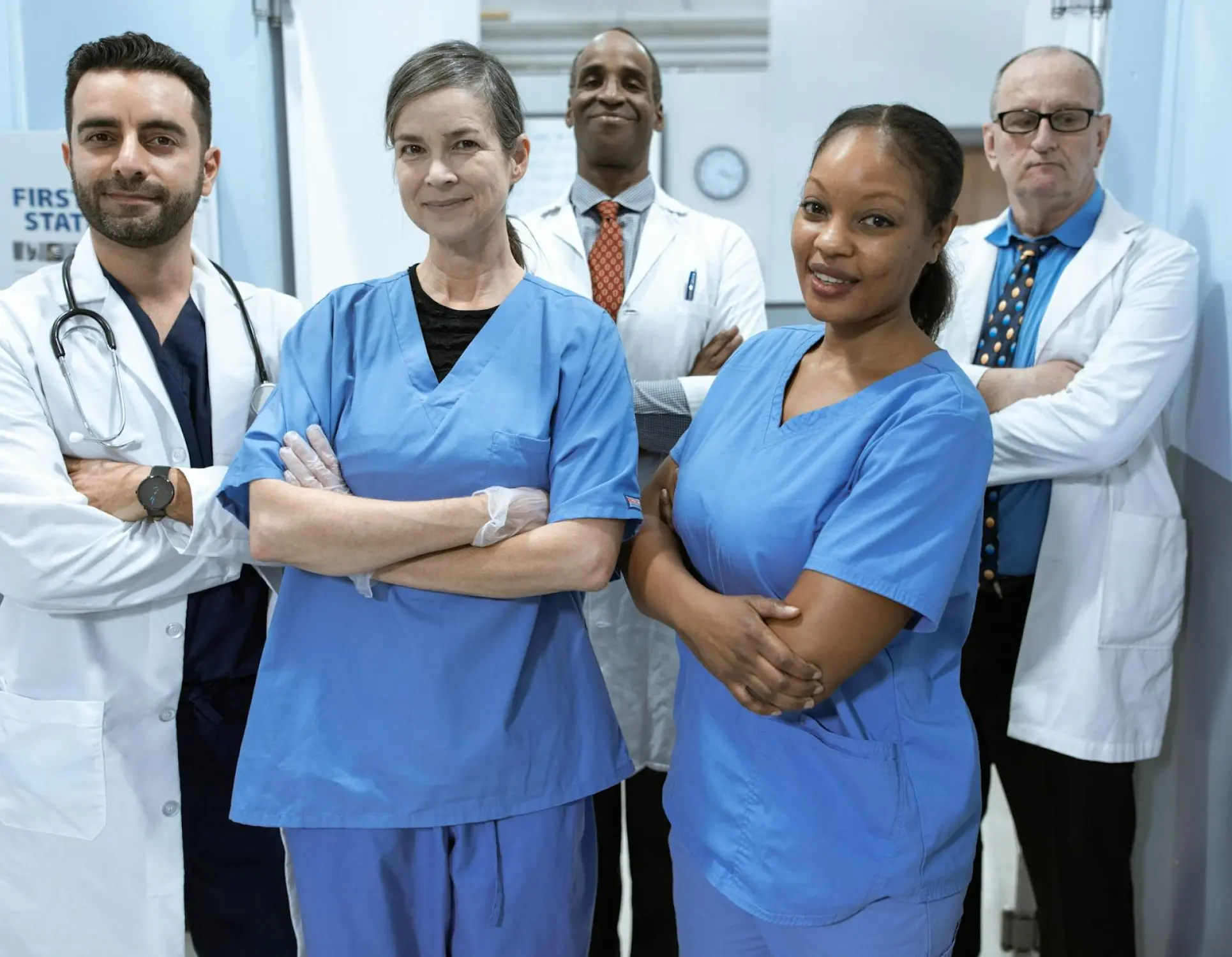 A group of five nurses, three males, two females, all standing with arms folded and smiling at the camera